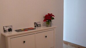 Eine weiße Kommode mit Schubladen, ein kleiner Vasen mit einer roten Blume und zwei schwarz-weiße Fotografien darauf.