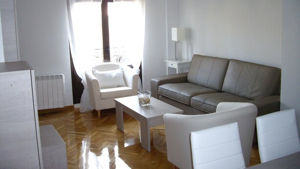 Ein modernes Wohnzimmer mit einer Couch, Sesseln, einem Couchtisch und einer Lampe.