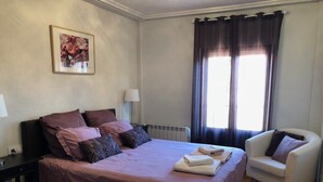 Ein Schlafzimmer mit einem großen Bett, einem Sessel, einer Heizung und einem Fenster mit Vorhängen.