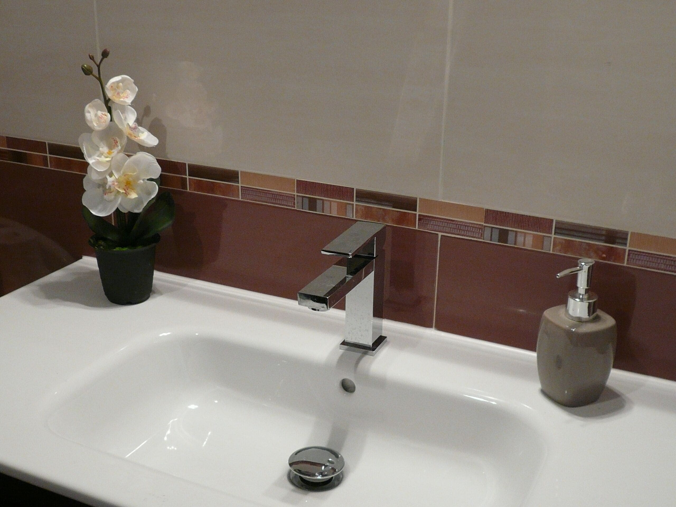 Un lavamanos de baño con un grifo moderno, un dispensador de jabón y una orquídea en maceta.
