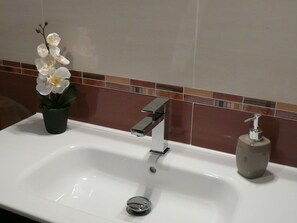 Un lavabo de salle de bain doté d’un robinet moderne, d’un distributeur de savon et d’une orchidée en pot.