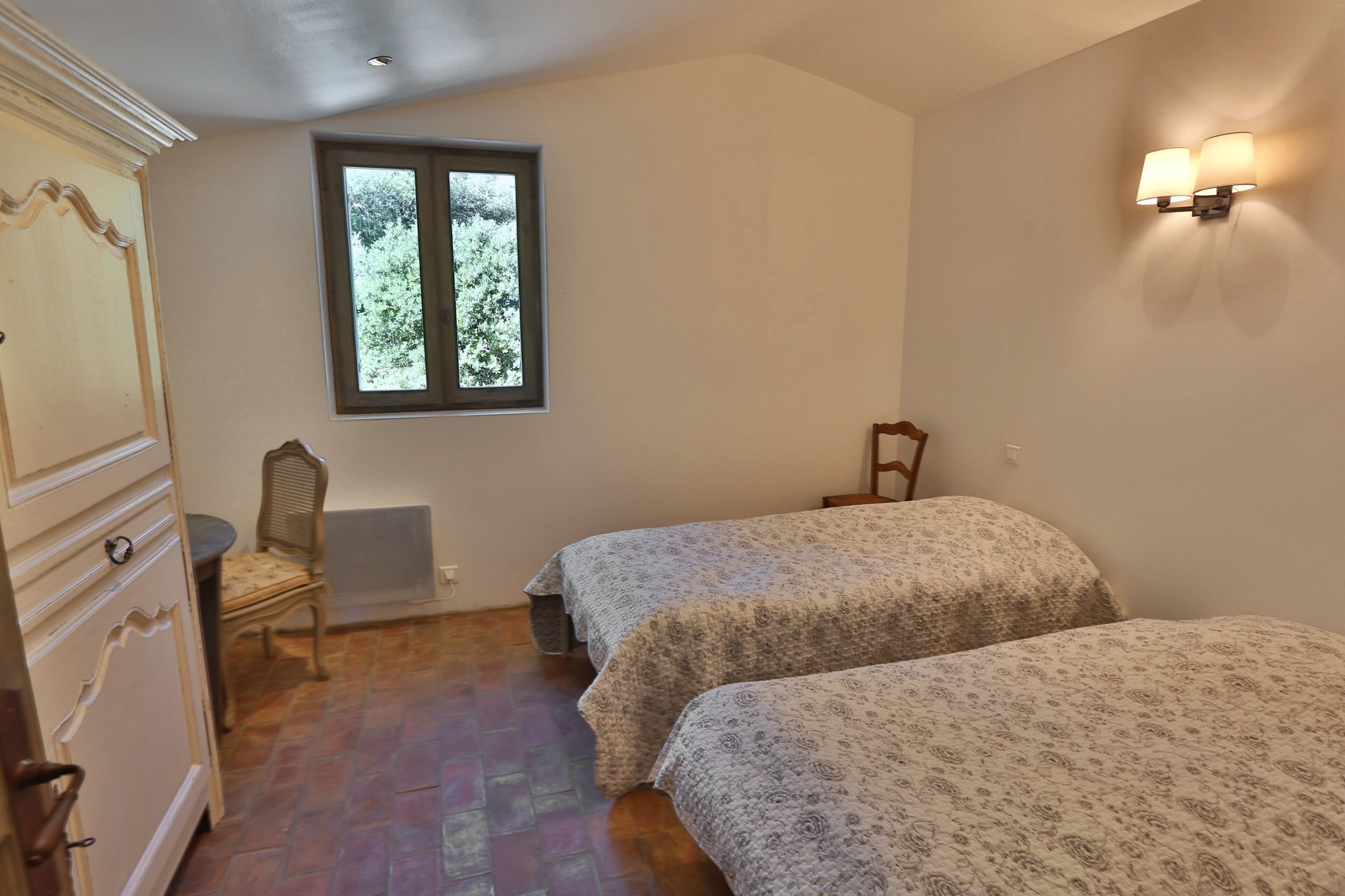 Quarto com duas camas, uma janela, uma cadeira e um armário.