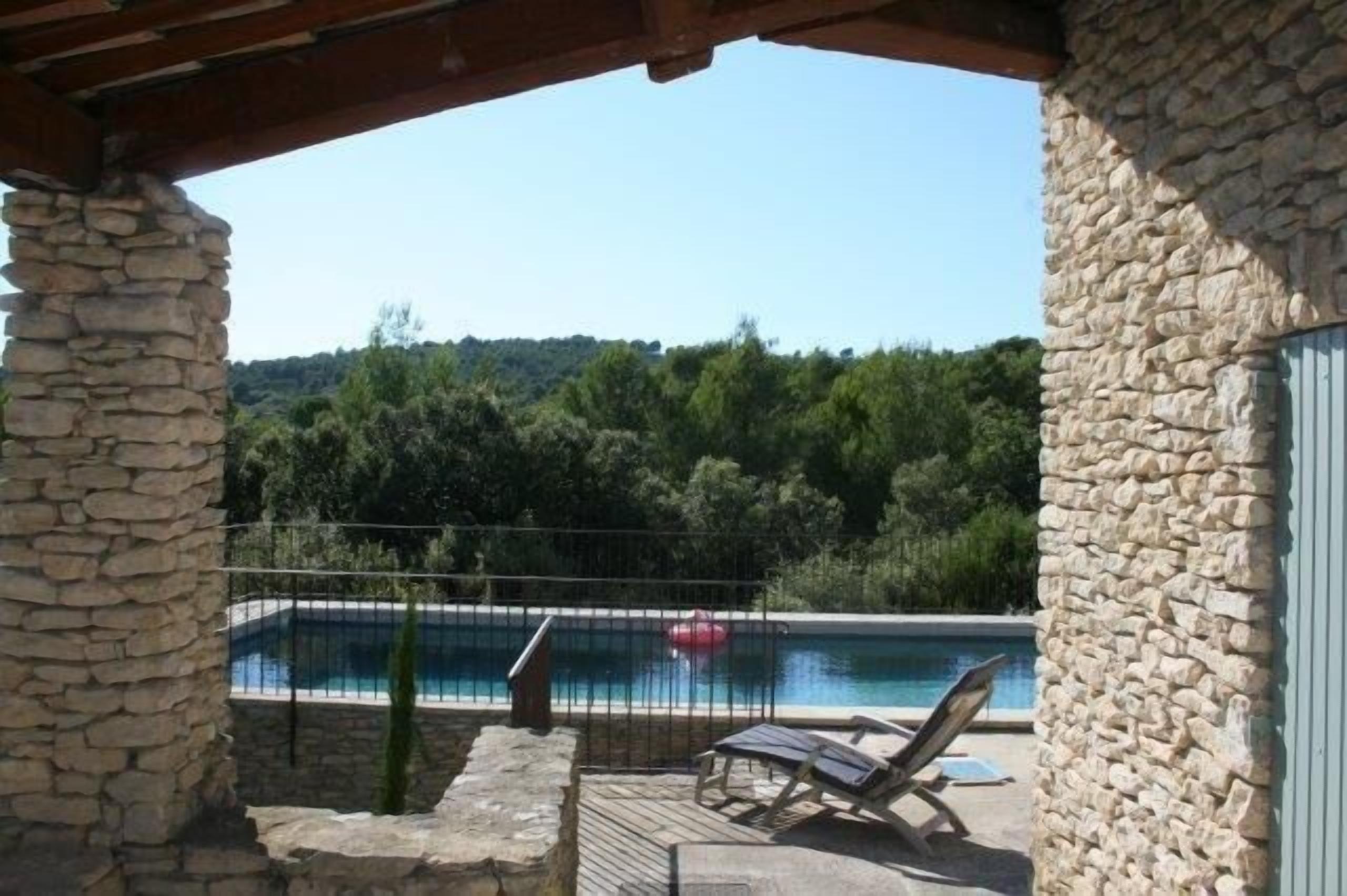 A stone-walled balcony with a pool, lounge chairs, and a view of a forested hillside.