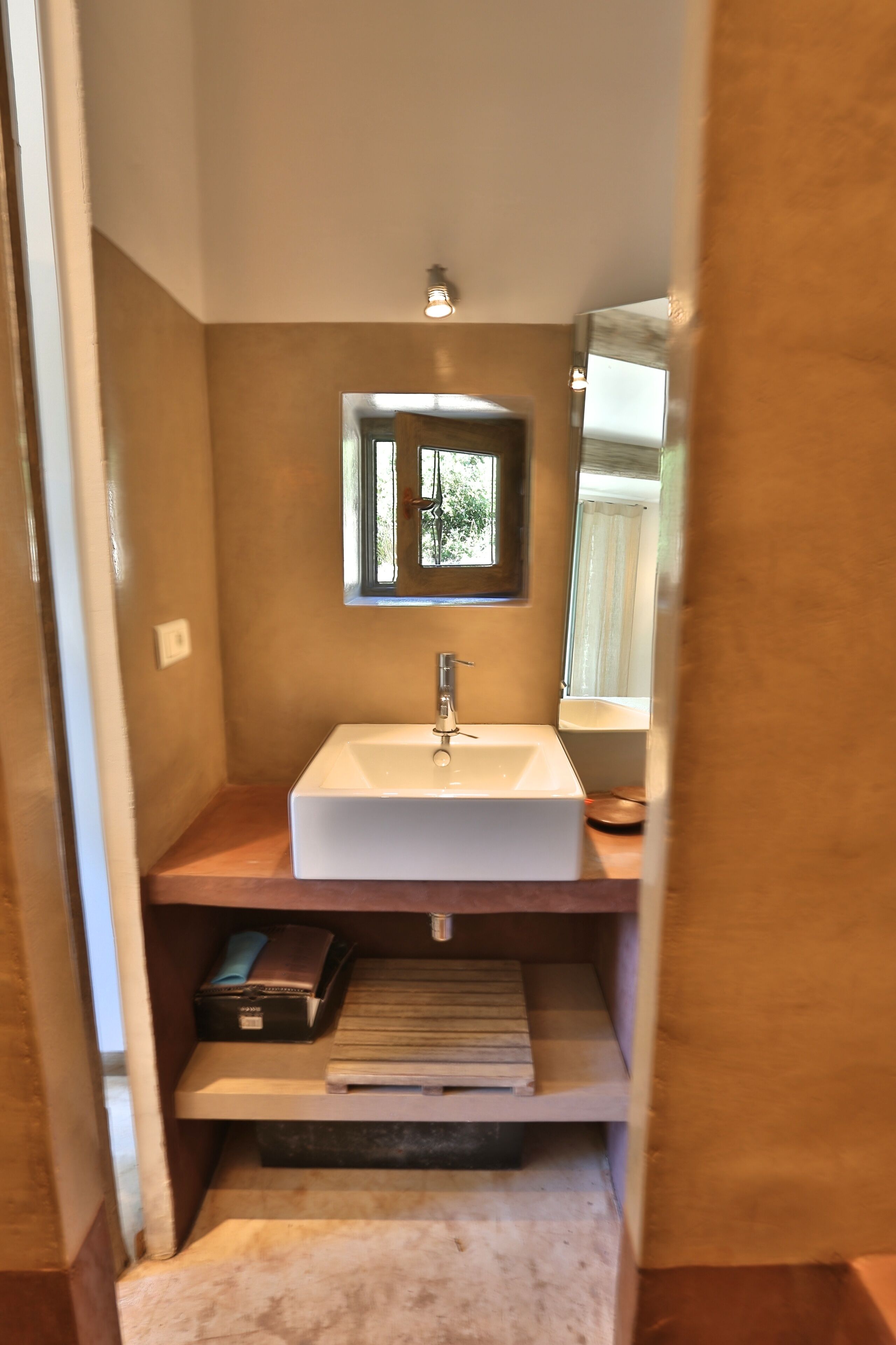 A compact bathroom with a white sink, a mirror above it, and a window providing natural light.