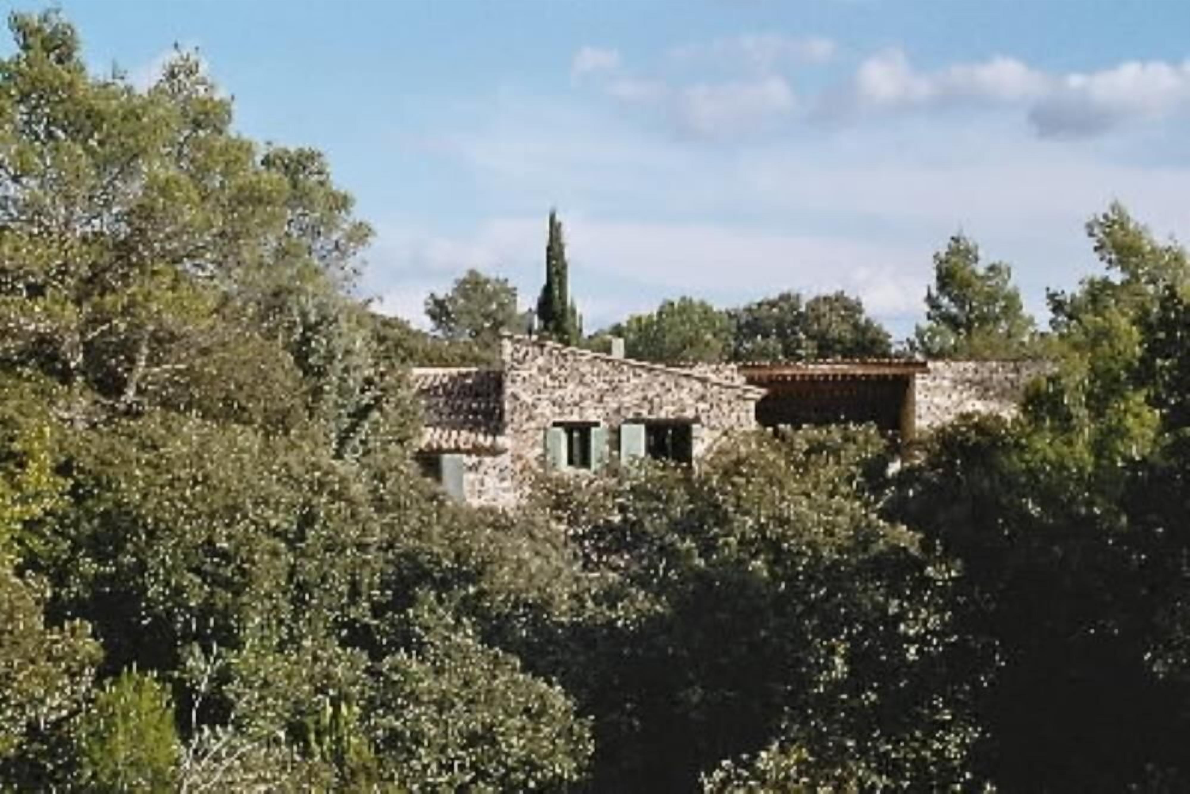 Un bâtiment en pierre, surmonté d’un toit en tuiles, entouré d’une végétation luxuriante.