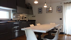 Una cocina moderna con armarios oscuros, una mesa de comedor blanca y dos sillas blancas con cojines negros. Hay tres lámparas colgantes sobre la mesa.