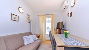 Une pièce confortable avec un canapé, une table à manger et des chaises, un téléviseur et une fenêtre avec des rideaux.