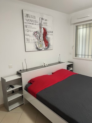 A modern bedroom with a bed, bedside tables, a red throw, and a wall art piece.