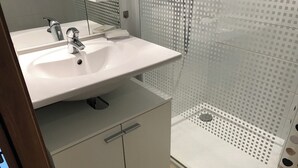 A bathroom with a white sink, two faucets, a mirror, and a shower with a perforated glass door.