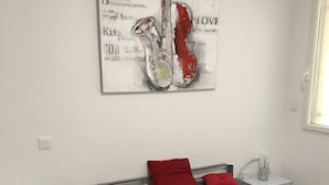 A bedroom with a bed, red pillows, a bedside table with a lamp, and a wall art piece.