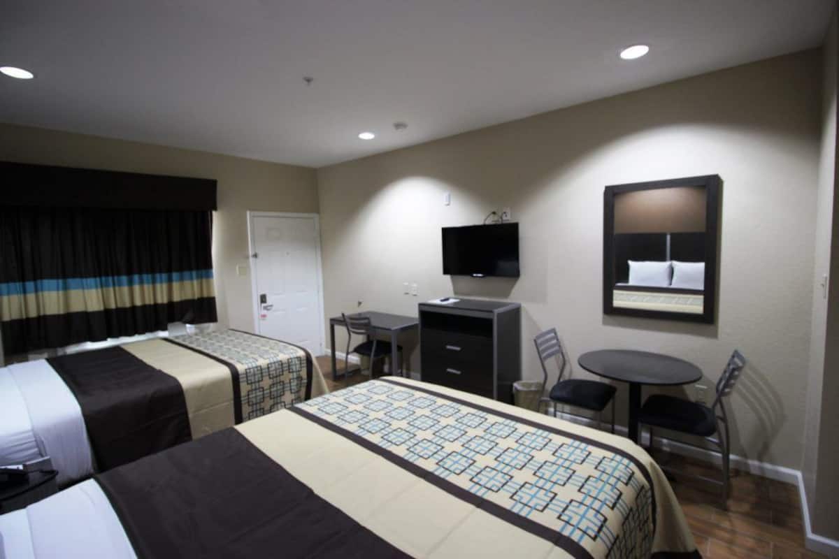 A hotel room with two beds, a desk, a chair, a television, and a small table.