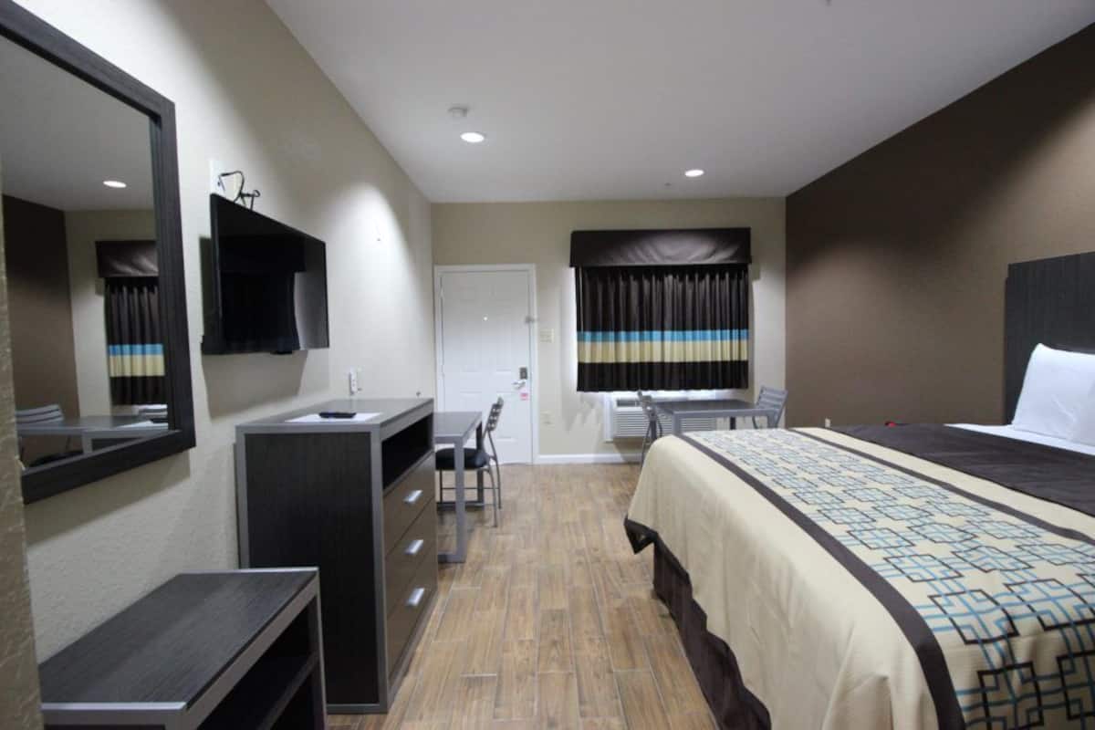 A hotel room with a bed, a desk, a chair, a mirror, and a wardrobe.