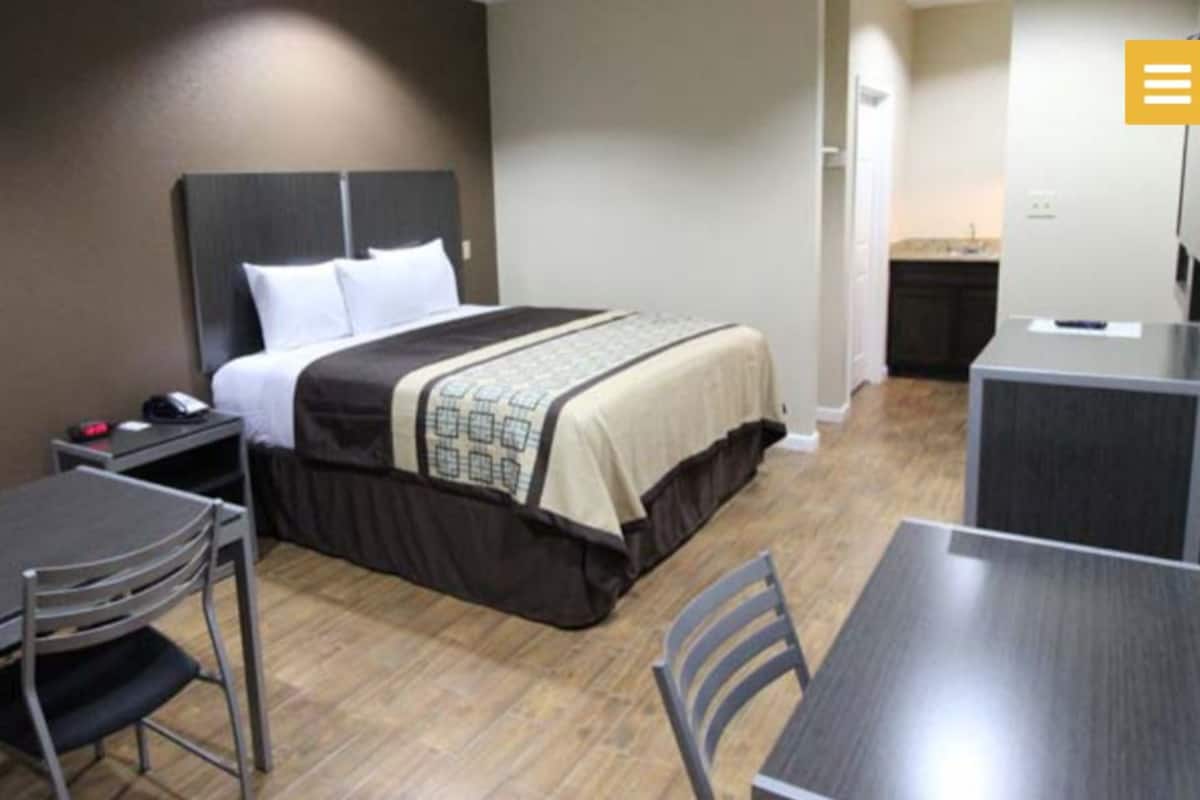 A hotel room with a bed, a desk, a chair, and a small table.