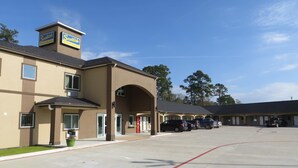 A motel with multiple units, a parking lot, and a clear sky. - Scottish Inn & Suites (Baytown)
