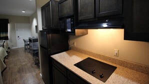 A compact kitchen with dark cabinetry, a built-in microwave, and a granite countertop. - Scottish Inn & Suites (Baytown)