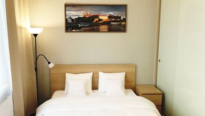 A hotel room with a bed, two pillows, a nightstand, a lamp, and a framed picture on the wall.