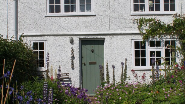 A white house with a red-tiled roof, a green door, and a garden with various flowers.