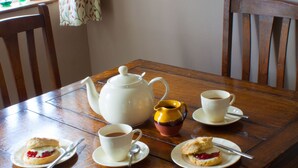 A wooden dining table with a white teapot, two cups, and two plates with scones and jam.