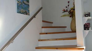 A staircase with wooden steps and a metal handrail, leading to a landing with a vase of flowers and a small shelf with books. - Lovely, two bedroom, air-conditioned Town House, set on a wonderful development (Paphos)