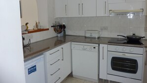 A compact kitchen with white cabinetry, a dishwasher, an oven, and a toaster. - Lovely, two bedroom, air-conditioned Town House, set on a wonderful development (Paphos)