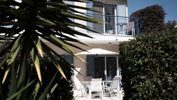A two-story house with a balcony, white outdoor furniture, and a large umbrella. - Lovely, two bedroom, air-conditioned Town House, set on a wonderful development (Paphos)