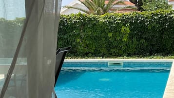 Relax by the serene pool, surrounded by a neatly trimmed hedge and a tiled patio.