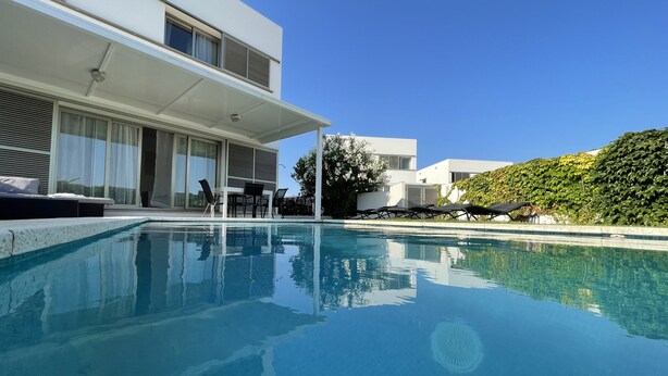 A modern pool area with a clear blue pool, lounge chairs, and a dining area with outdoor furniture.