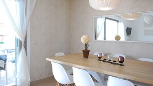 A dining area with a wooden table, white chairs, a vase with flowers, and a mirror on the wall.