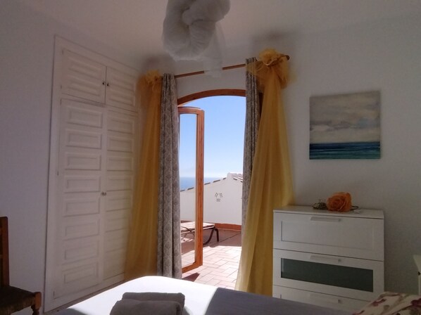 A bedroom with a bed, a dresser, and a view of the beach through a doorway.