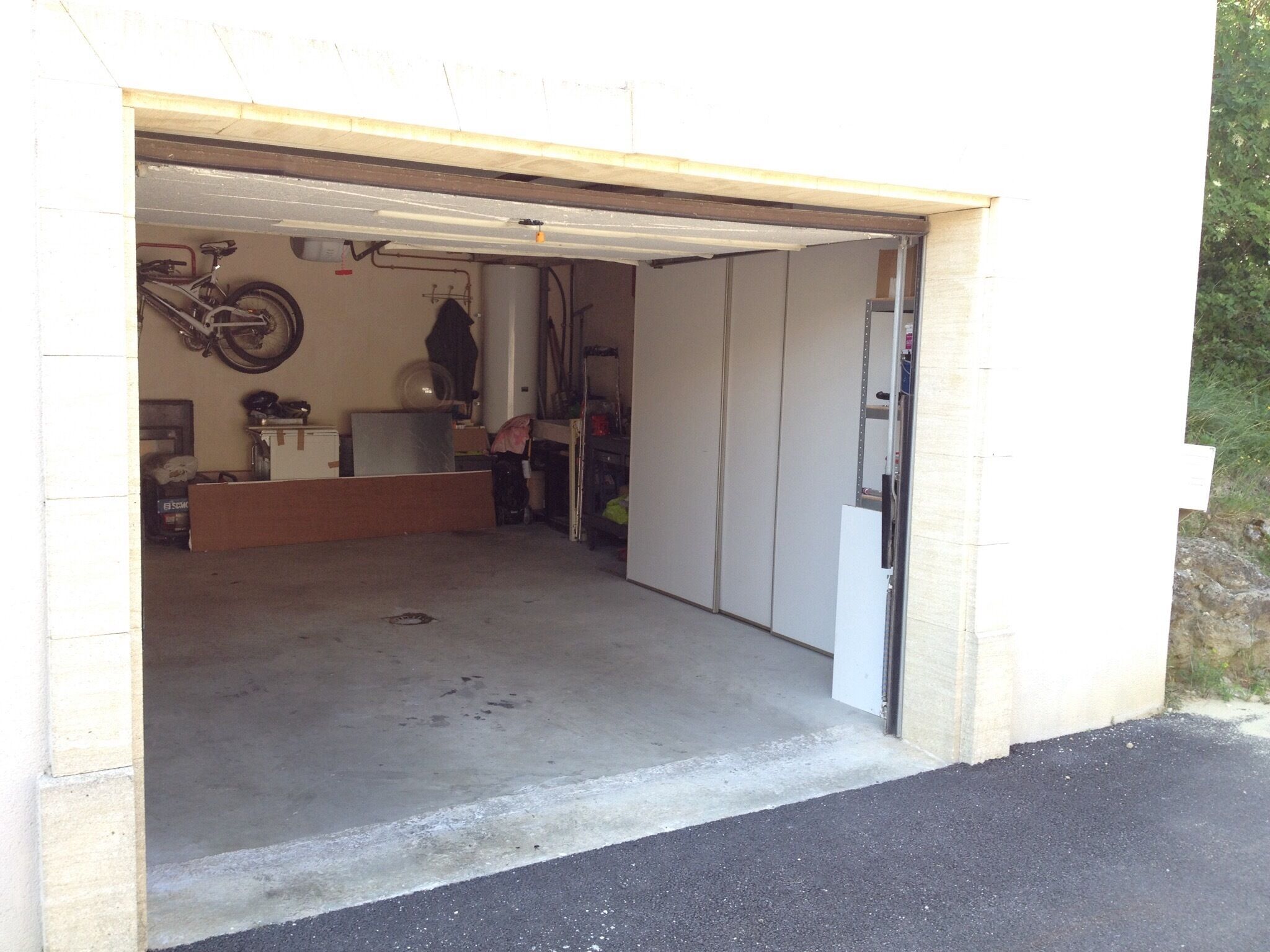Un garage contenant un vélo, un ventilateur et divers objets rangés le long des murs.