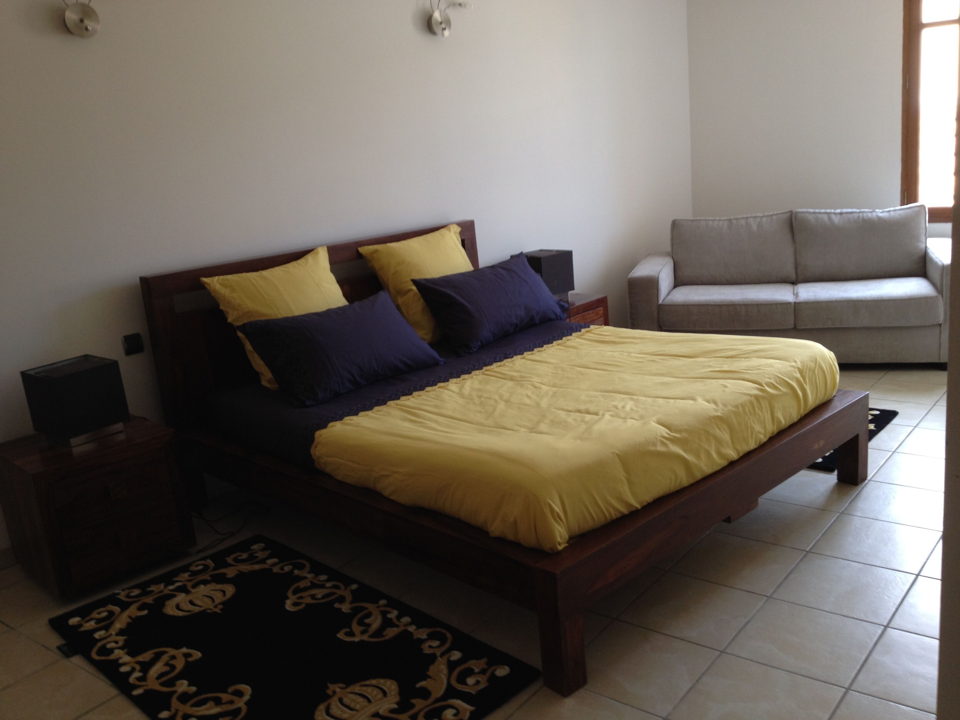 A bedroom with a bed, bedside tables, a sofa, and a patterned rug.