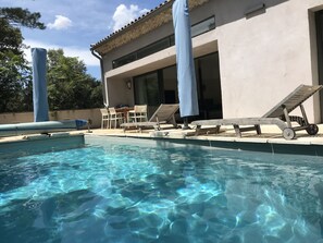 A swimming pool with clear water, surrounded by lounge chairs and a table. - At the top of the village, magnificent view of Mt Ventoux, private heated swimming pool (Bédoin)