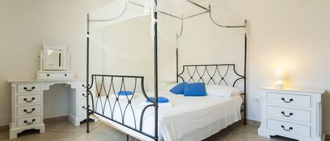 Una cama con dosel y cortinas, una mesita de noche con lámpara, y un aparador con cajones.