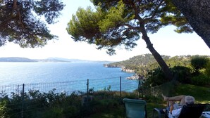 Vista costanera amb una cadira i una taula sota un arbre, amb vista al mar.