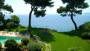 Un jardí paisatjístic amb piscina, gandules i vistes al mar.