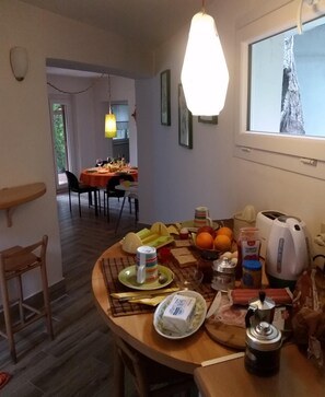 Un coin repas avec une table dressée pour deux personnes, une bouilloire, des condiments et une fenêtre donnant sur un beau paysage.