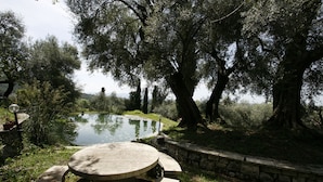 A stone bench and table set in a garden with a pond and trees.