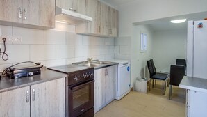 Kompakti keittiö, jossa on puukalusteet, sisäänrakennettu uuni, astianpesukone ja pieni ruokailutila, jossa on pöytä ja tuolit.