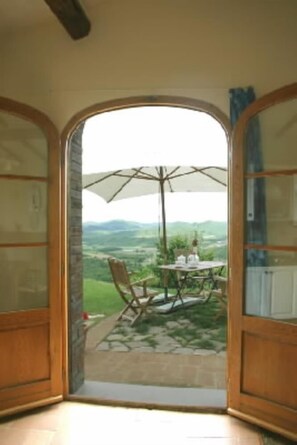 An open doorway leading to an outdoor patio with a table and chairs, a large umbrella, and a view of a green landscape. - Detached villa with a panoramic garden (Chiusdino)