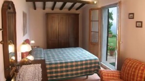 Una habitación con cama, una silla, un armario de madera y una puerta que da a un jardín.