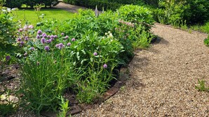 A garden pathway with gravel, surrounded by lush greenery and flowering plants. - Peaceful, Picturesque, Stylish Property in Benenden Converted Barn (Cranbrook Rd)