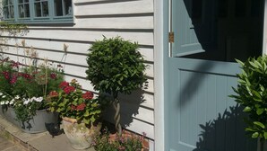 A white building with a blue door and windows. There are potted plants and flowers along the side. - Peaceful, Picturesque, Stylish Property in Benenden Converted Barn (Cranbrook Rd)