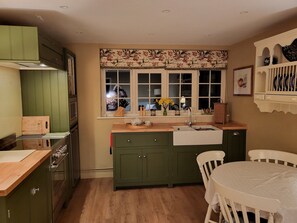 A kitchen with green cabinets, a wooden countertop, a sink, and a window with floral curtains. - Peaceful, Picturesque, Stylish Property in Benenden Converted Barn (Cranbrook Rd)