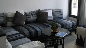 A modern living room with a sectional sofa, a small round table, and two wall-mounted light fixtures. - House with character (Azemmour)