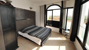 A bedroom with a bed, a wardrobe, a window with curtains, and a view of the landscape. - House with character (Azemmour)