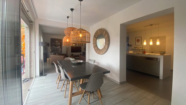 Un espace repas moderne avec une table en bois foncé, des chaises gris clair et un luminaire suspendu au centre.