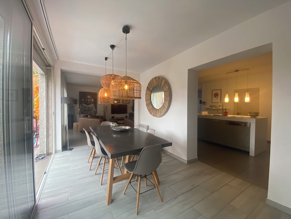 Un espace repas moderne avec une table en bois foncé, des chaises gris clair et un luminaire suspendu au centre.