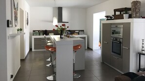 Une cuisine moderne dotée d’un îlot central, de meubles blancs et d’appareils électroménagers en acier inoxydable.
