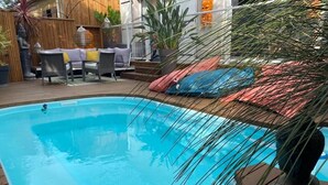 Une piscine dotée d’une terrasse en bois, entourée de meubles d’extérieur et de plantes.