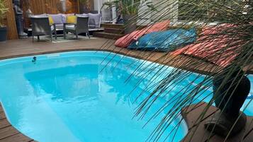Une piscine dotée d’une terrasse en bois, entourée de meubles d’extérieur et de plantes.